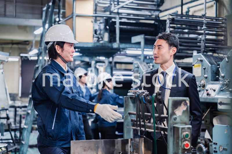 機械の前で話をする営業マンと労働者