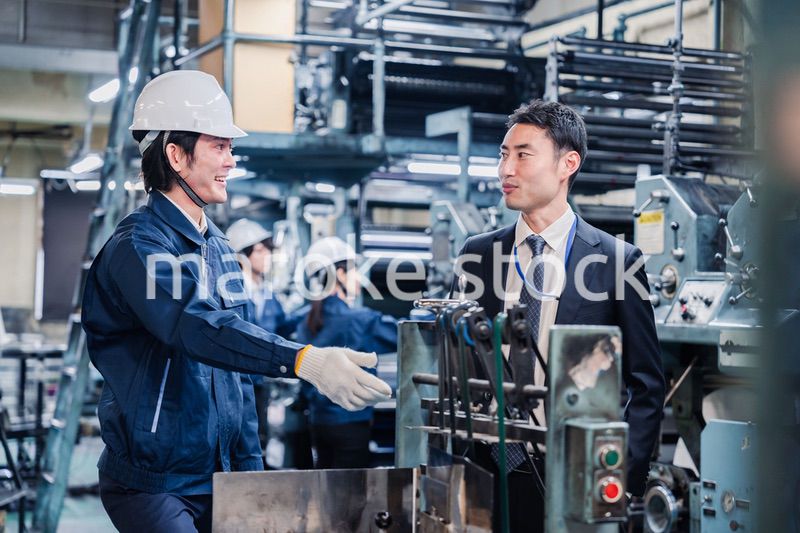 機械の前で話をする営業マンと労働者