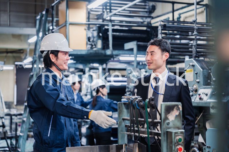 機械の前で話をする営業マンと労働者
