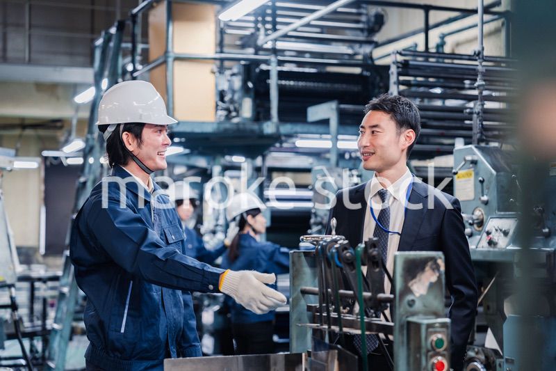 機械の前で話をする営業マンと労働者