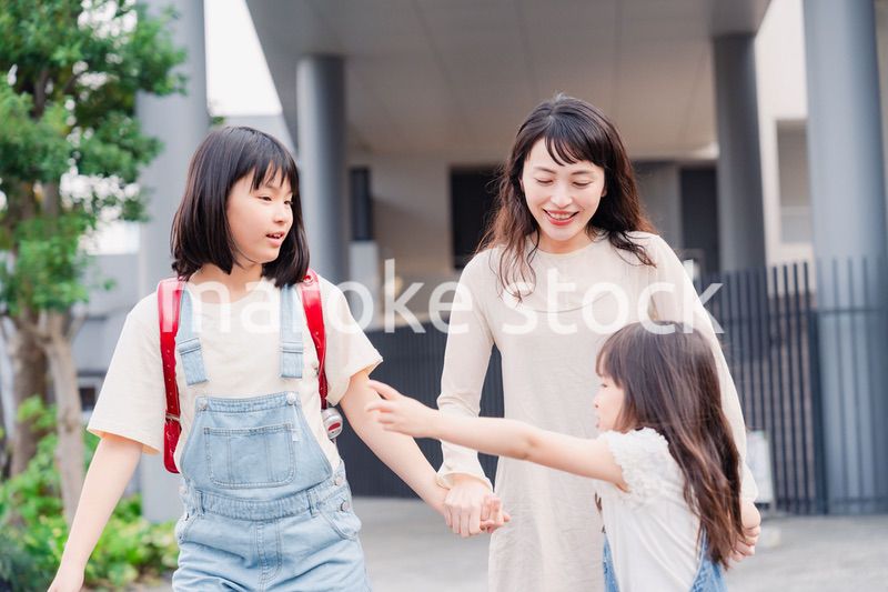 お母さんと手を繋いで学校に行く2人の女の子