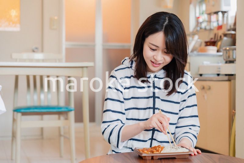 家でひとりでコンビニ弁当を食べる若い女性