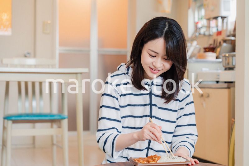 家でひとりでコンビニ弁当を食べる若い女性
