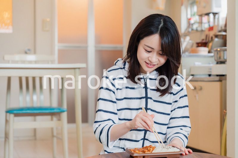 家でひとりでコンビニ弁当を食べる若い女性