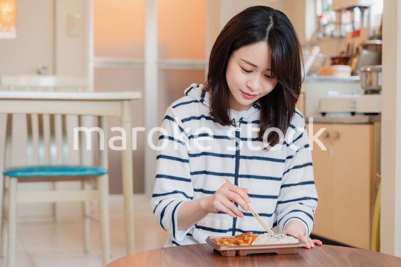 家でひとりでコンビニ弁当を食べる若い女性