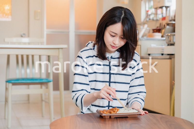 家でひとりでコンビニ弁当を食べる若い女性