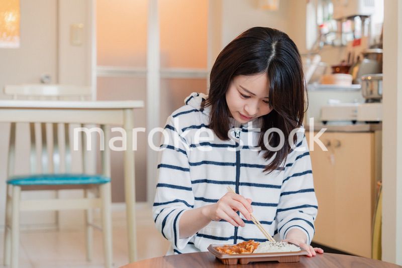 家でひとりでコンビニ弁当を食べる若い女性
