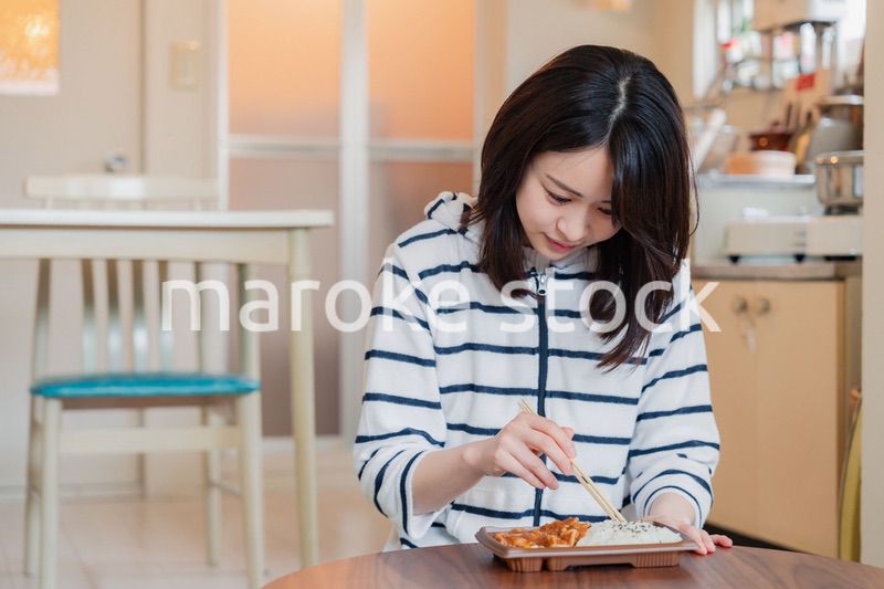 家でひとりでコンビニ弁当を食べる若い女性