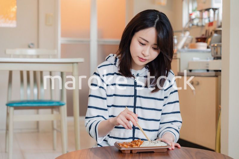 家でひとりでコンビニ弁当を食べる若い女性