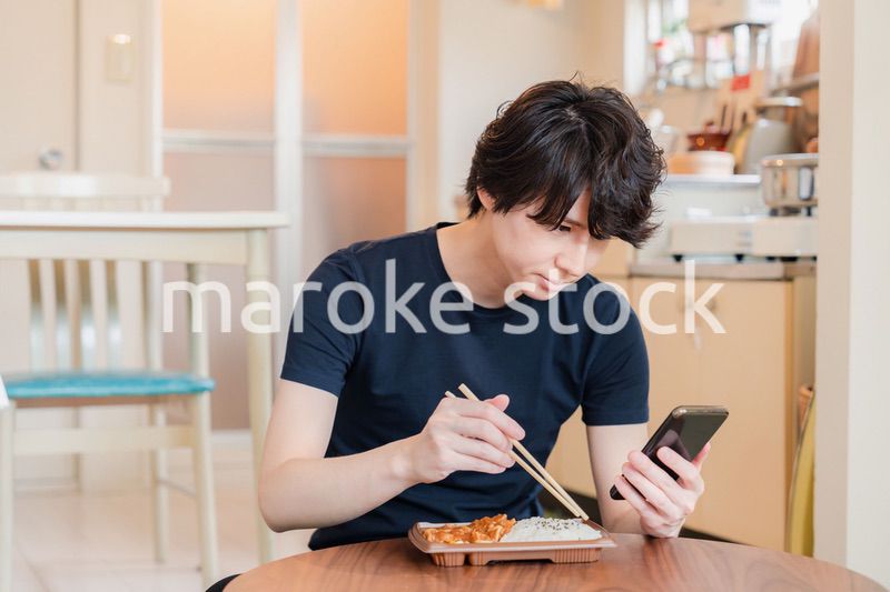 家でコンビニ弁当を食べる若い男性