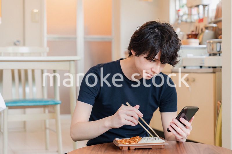家でコンビニ弁当を食べる若い男性