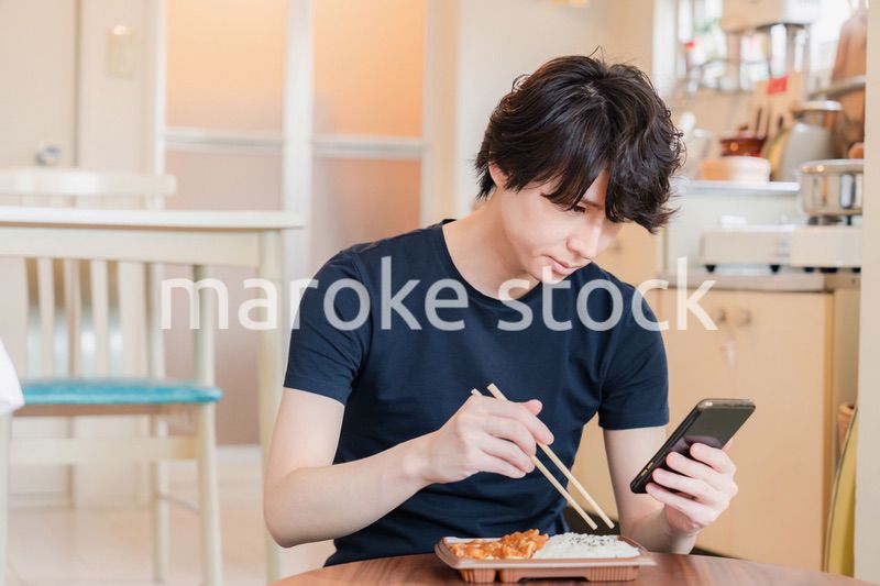 家でコンビニ弁当を食べる若い男性