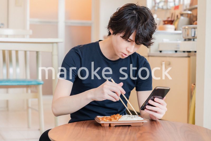 家でコンビニ弁当を食べる若い男性