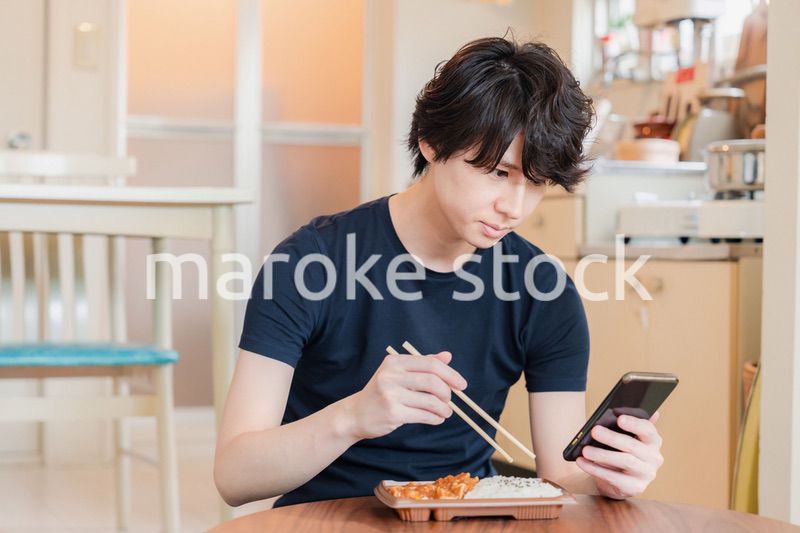 家でコンビニ弁当を食べる若い男性