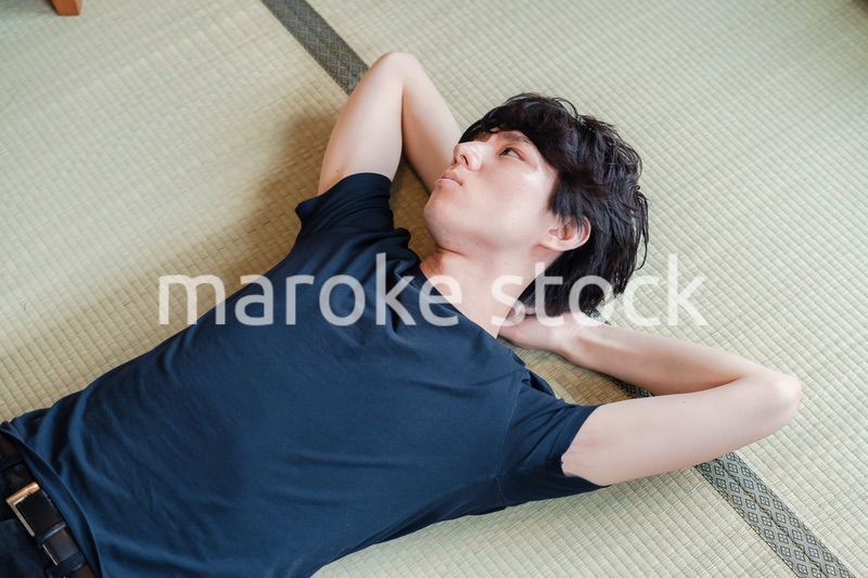 畳の上で寝転がる若い男性