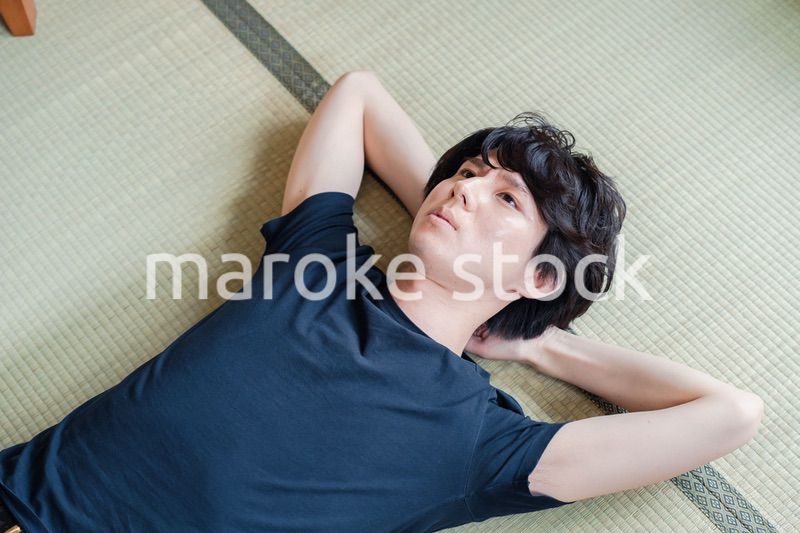 畳の上で寝転がる若い男性