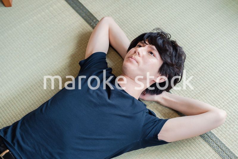 畳の上で寝転がる若い男性