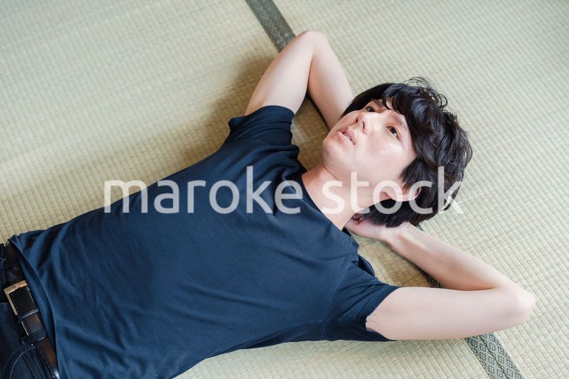 畳の上で寝転がる若い男性