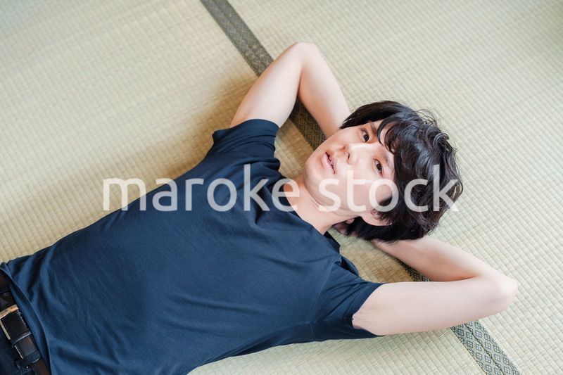 畳の上で寝転がる若い男性
