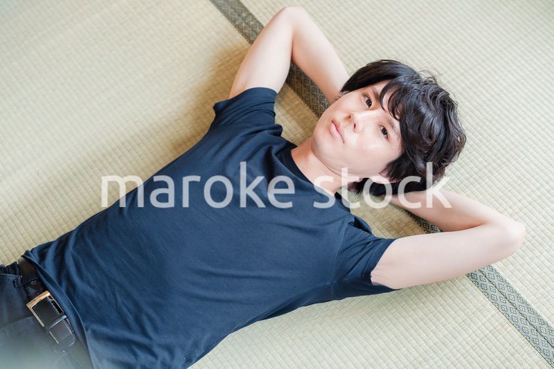 畳の上で寝転がる若い男性