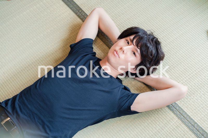 畳の上で寝転がる若い男性