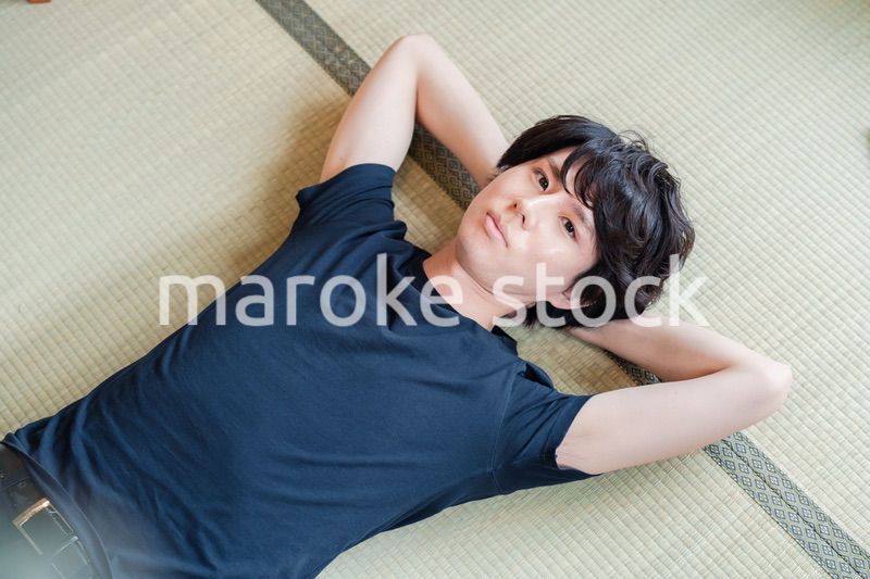 畳の上で寝転がる若い男性