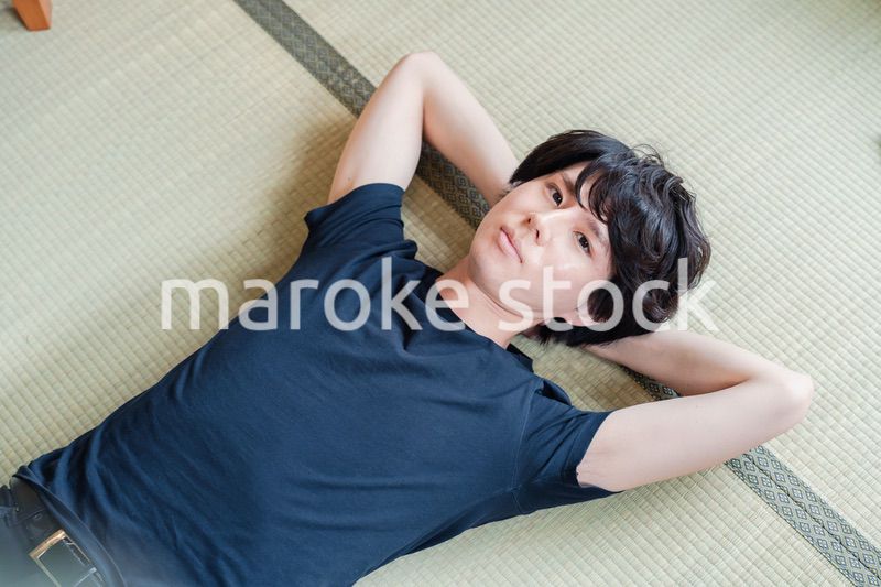 畳の上で寝転がる若い男性