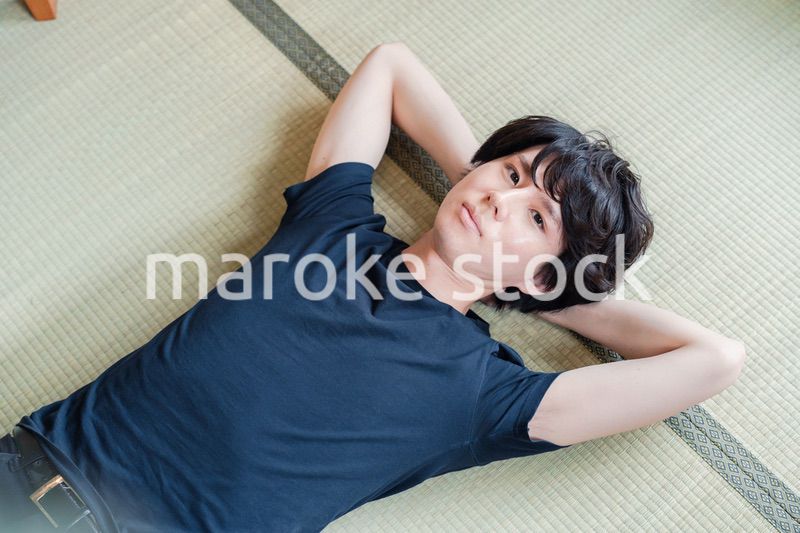 畳の上で寝転がる若い男性