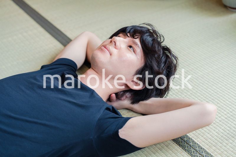 畳の上で寝転がる若い男性