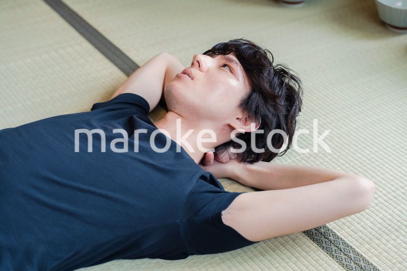 畳の上で寝転がる若い男性