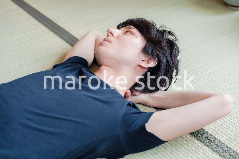 畳の上で寝転がる若い男性