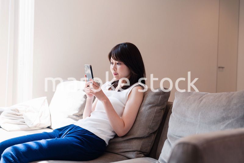 ソファでリラックスしてスマホを使う若い女性
