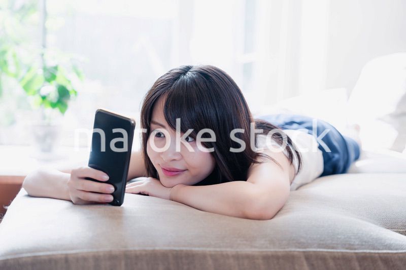 ソファでリラックスしてスマホを使う若い女性