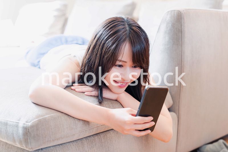 ソファでリラックスしてスマホを使う若い女性