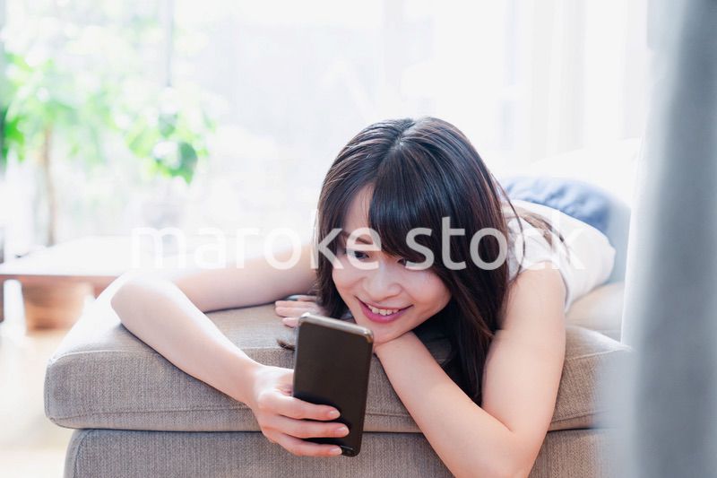 ソファでリラックスしてスマホを使う若い女性