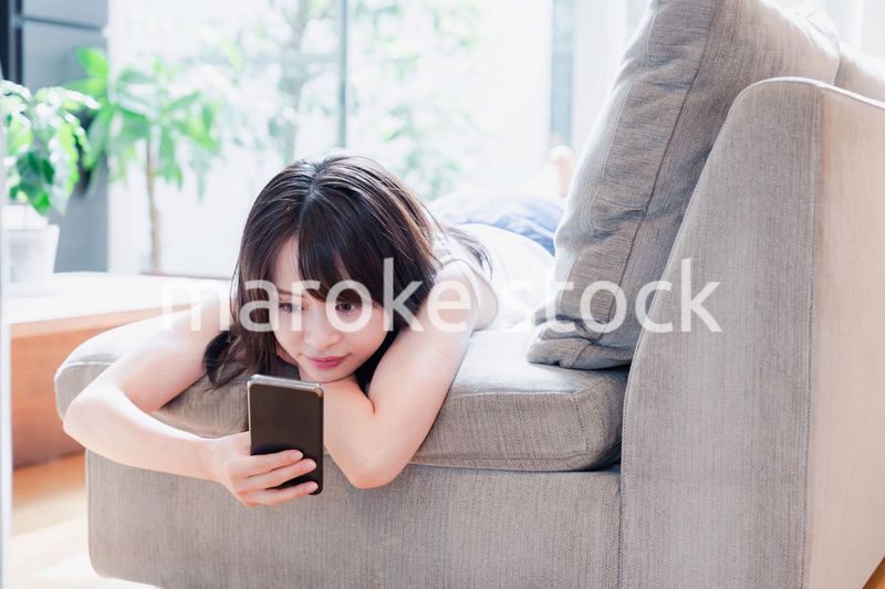 ソファでリラックスしてスマホを使う若い女性