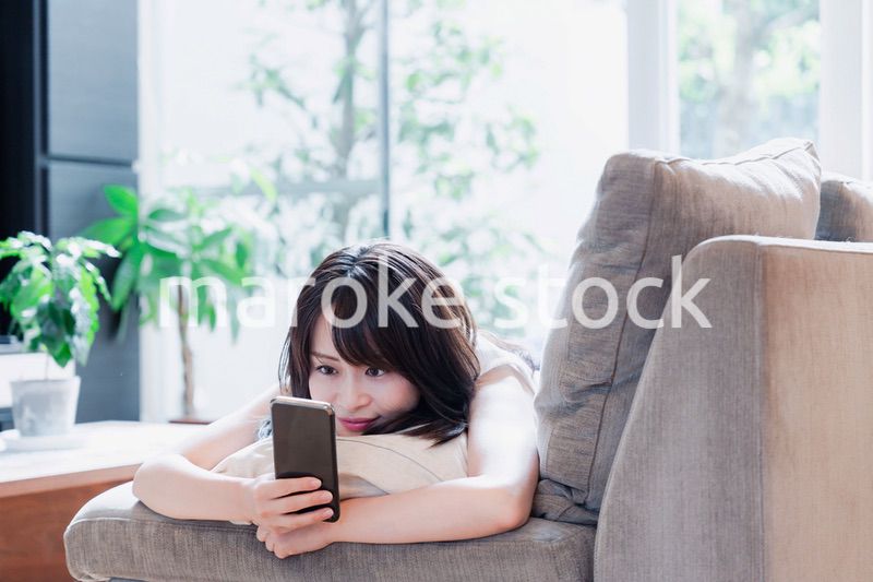 ソファでリラックスしてスマホを使う若い女性