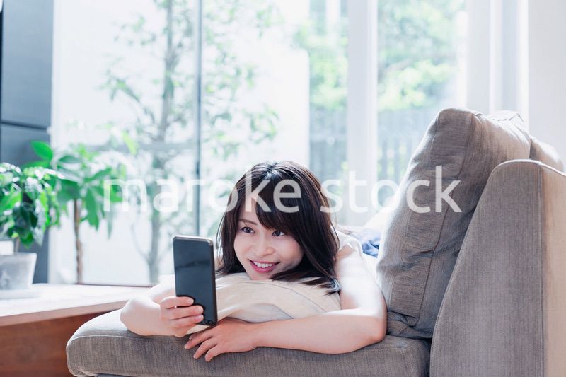 ソファでリラックスしてスマホを使う若い女性