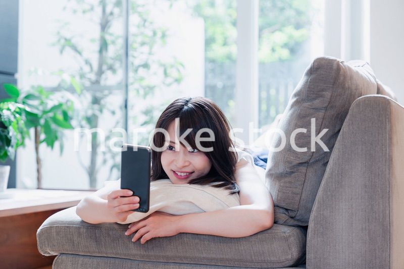 ソファでリラックスしてスマホを使う若い女性