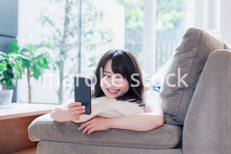 ソファでリラックスしてスマホを使う若い女性