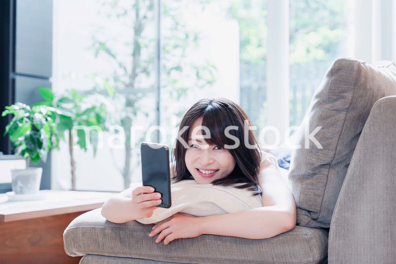 ソファでリラックスしてスマホを使う若い女性