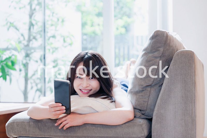 ソファでリラックスしてスマホを使う若い女性