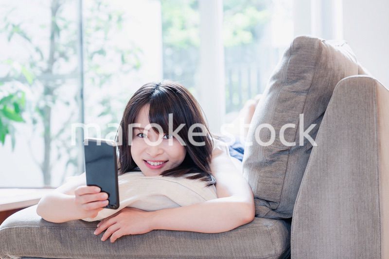 ソファでリラックスしてスマホを使う若い女性