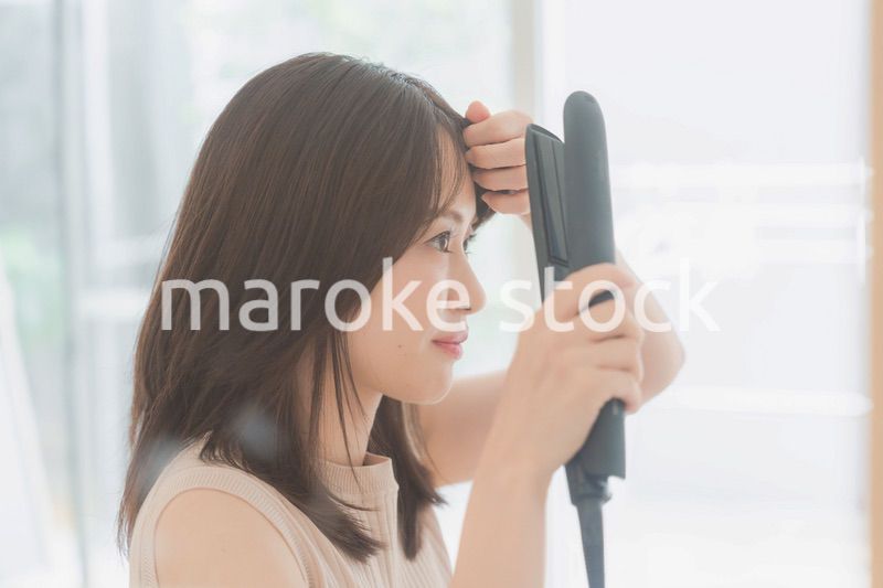 ヘアアイロンを使って髪をセットする若い女性