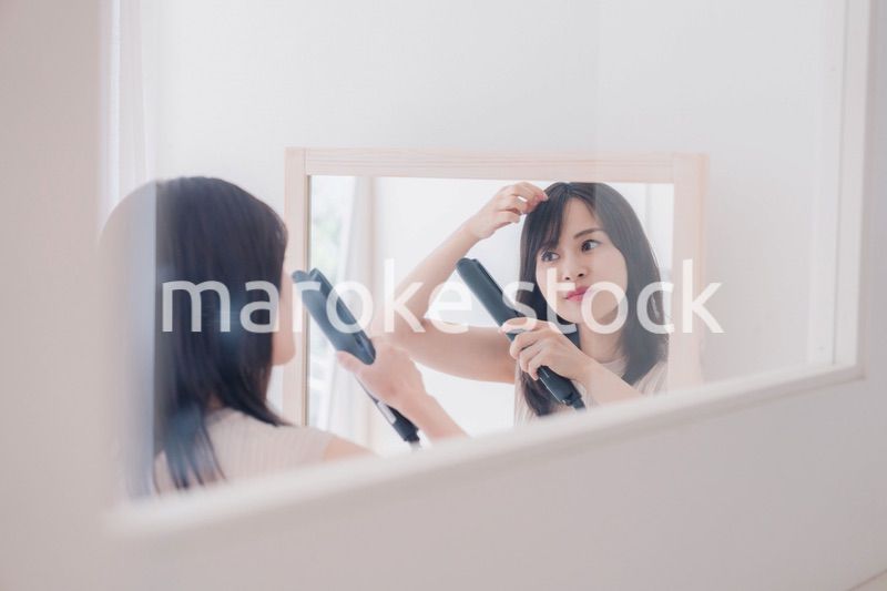 ヘアアイロンを使って髪をセットする若い女性