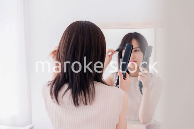 ヘアアイロンを使って髪をセットする若い女性