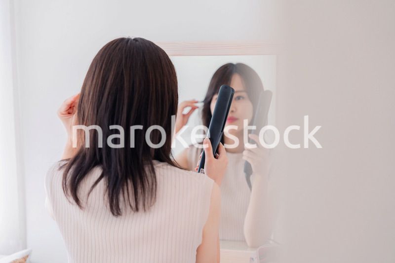 ヘアアイロンを使って髪をセットする若い女性