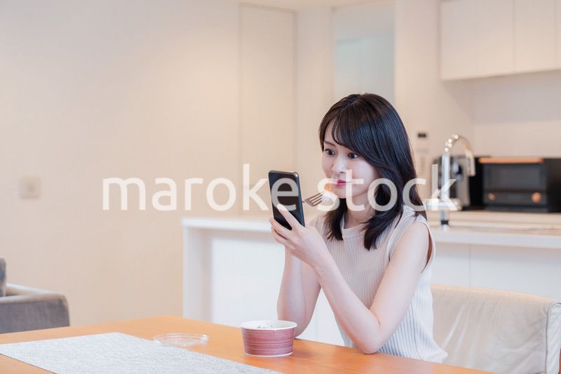 家でスマホを使いながらごはんを食べる若い女性