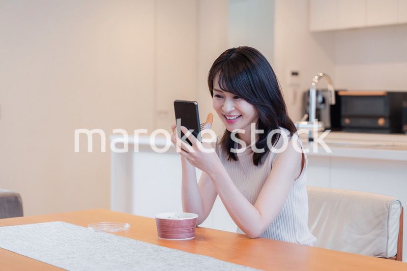 家でスマホを使いながらごはんを食べる若い女性