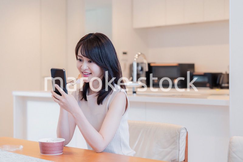 家でスマホを使いながらごはんを食べる若い女性